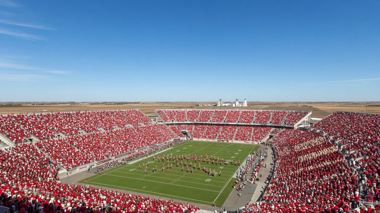 Sold-out college football stadium on a bright midday in the Great Plains, a sea of red in the stands under a big blue sky