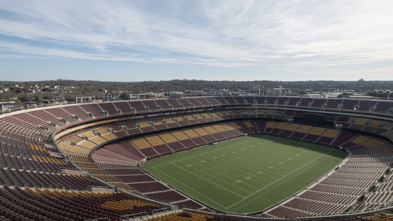 Empty open-air football stadium surrounded by bare autumn trees under a cool December sky, no people
